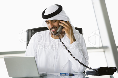 A Middle Eastern businessman using a phone and laptop