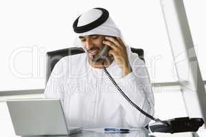 A Middle Eastern businessman using a phone and laptop