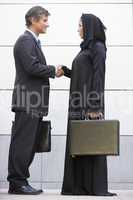 A Middle Eastern businesswoman shaking hands with a Caucasian businessman