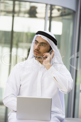 A Middle Eastern businessman using a mobile phone and laptop