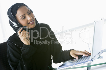 A Middle Eastern businesswoman using a laptop and phone headset