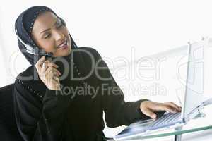 A Middle Eastern businesswoman using a laptop and phone headset