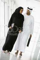 A Middle Eastern businessman and businesswoman walking down a co