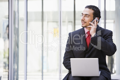 Businessman using laptop and mobile phone outside