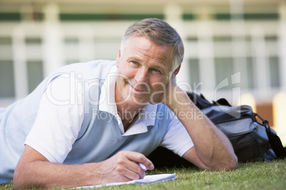 A man writing notes while lying on a campus lawn