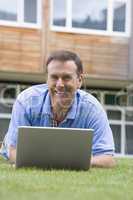 Man using laptop while lying in grass on campus