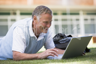 Man using laptop while lying in grass on campus