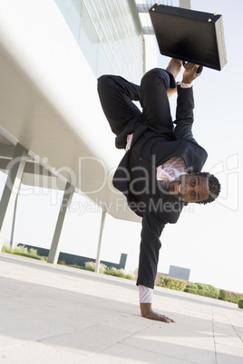 Businessman outdoors by building standing on one hand smiling