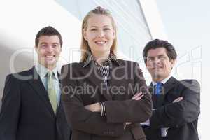 Three businesspeople standing outdoors by building smiling