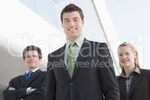 Three businesspeople standing outdoors by building smiling