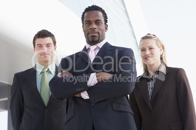 Three business people standing outdoors by building smiling