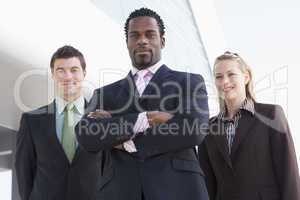 Three business people standing outdoors by building smiling