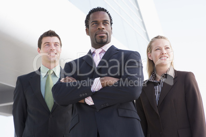 Three business people standing outdoors by building smiling