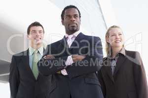 Three business people standing outdoors by building smiling