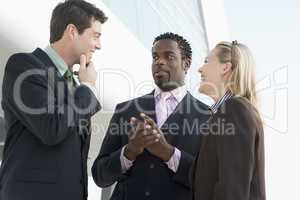 Three businesspeople standing outdoors by building talking and s