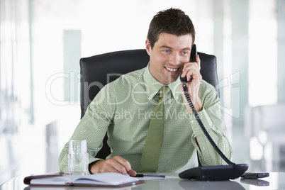 Businessman sitting in office with personal organizer on telepho