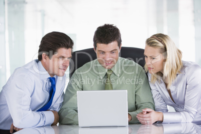 Three businesspeople in a boardroom looking at laptop