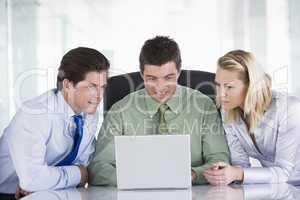 Three businesspeople in a boardroom looking at laptop