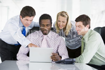 Four businesspeople in a boardroom pointing at laptop and smilin