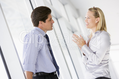 Businessman standing in corridor talking to smiling businesswoma