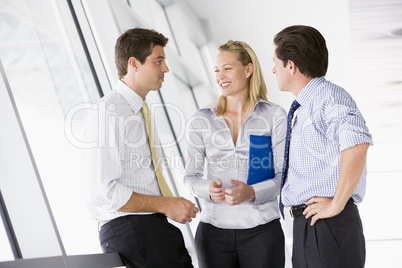 Three businesspeople standing in corridor talking and smiling