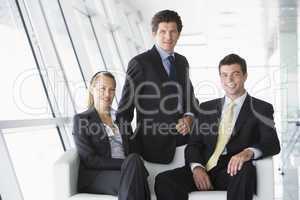 Three businesspeople sitting in office lobby smiling