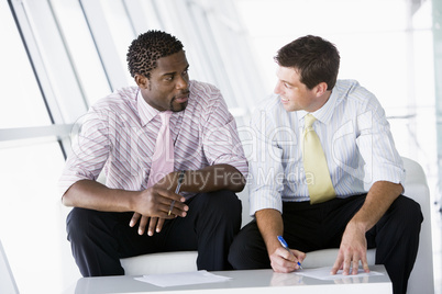 Two businessmen sitting in office lobby talking and smiling
