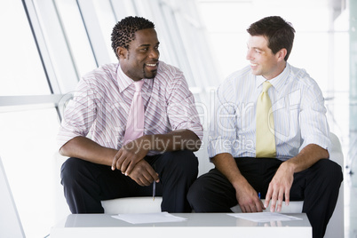 Two businessmen sitting in office lobby talking and smiling