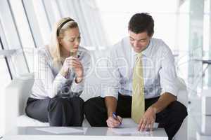 Two businesspeople sitting in office lobby talking and smiling