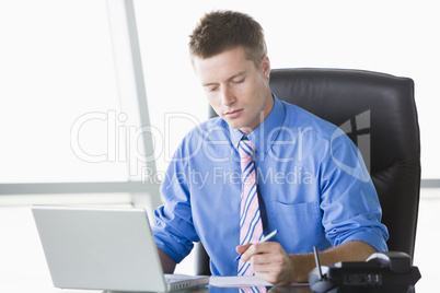 Businessman sitting in office with laptop writing note