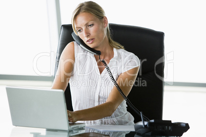 Businesswoman sitting in office with laptop on telephone