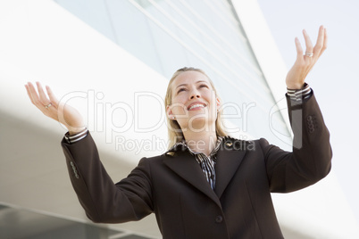 Businesswoman standing outdoors by building with hands out smili