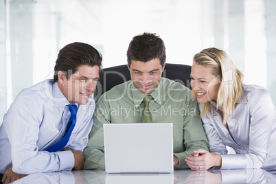 Three businesspeople in office with laptop smiling