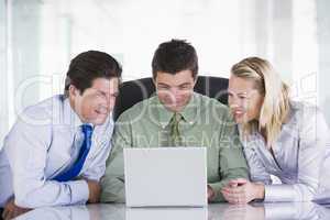 Three businesspeople in office with laptop smiling