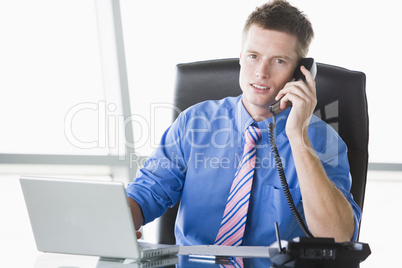 Businessman sitting in office with laptop using telephone