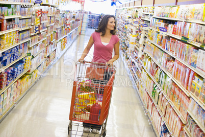 Woman pushing trolley along supermarket aisle