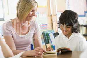 A schoolboy and his teacher reading a book in class
