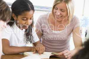 A schoolgirl and her teacher reading a book in class
