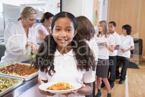 Schoolgirl holding plate of lunch in school cafeteria