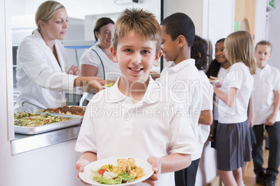 Schoolboy holding plate of lunch in school cafeteria