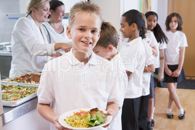 Schoolboy holding plate of lunch in school cafeteria
