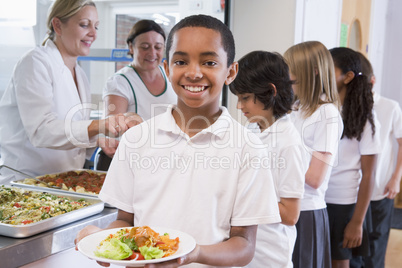 Schoolboy holding plate of lunch in school cafeteria