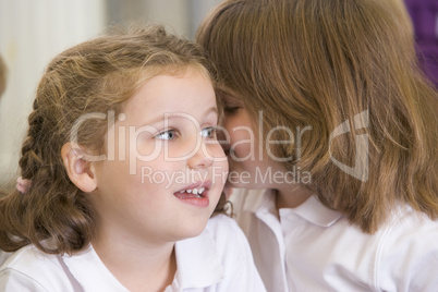A schoolgirl whispers to her friend in a primary class