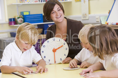Teacher helping schoolchildren learn to tell time in primary class