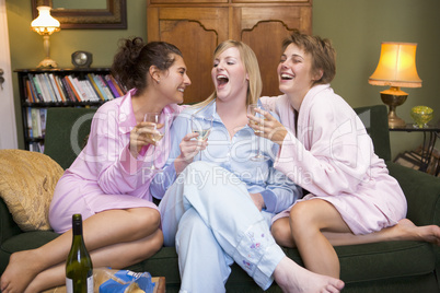 Drei Frauen sitzen im Morgenmantel und Pyjama auf dem Sofa und trinken Sekt