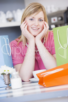 Blonde Frau sitzt am Tisch zwischen bunten Taschen