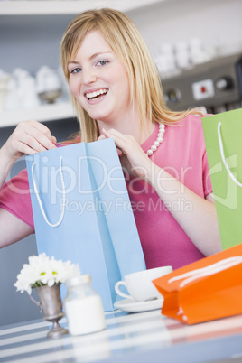 Blonde Frau sitzt am Tisch zwischen bunten Taschen