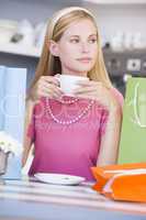Blonde Frau sitzt am Tisch und trinkt aus einer Tasse