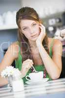 Junge dunkelhaarige Frau sitzt am Tisch vor weisser Tasse