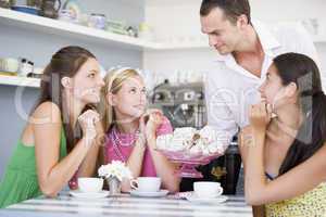 Drei junge Frauen sitzen in einem Cafè und werden von einem Kellner bedient